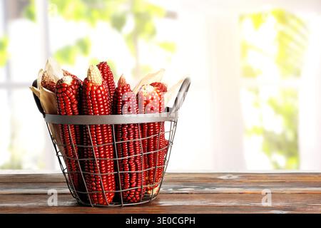 Red corn cobs in basket on wooden table indoors, space for text Stock Photo