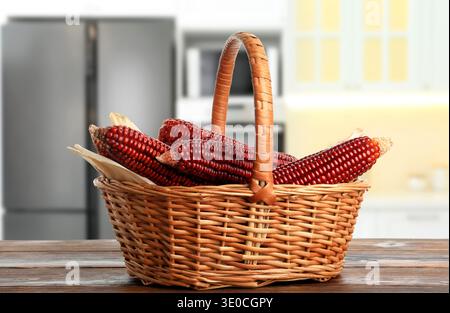 Red corn cobs in basket on wooden table in kitchen Stock Photo