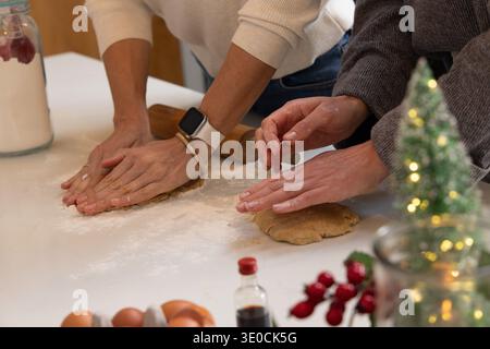 Two bakers pressing, shaping dough on flour-dusted kitchen counter in knit tops with rolling pin Stock Photo