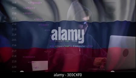 Typing hacker wearing hoodie and sunglasses on laptop at dim desk, with overlaid code and flag Stock Photo