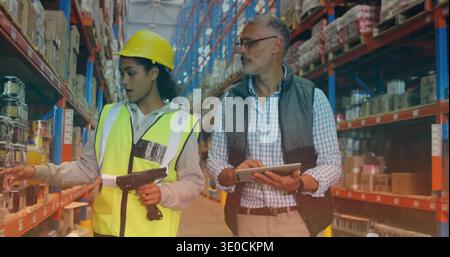 Scanning hi-vis vest worker and manager checking stock in warehouse bay, with scanner and tablet Stock Photo