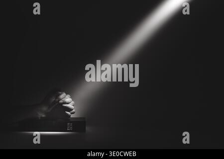 A strong beam of light illuminating a holy bible and the hands of a person praying, a background of faith and belief. Stock Photo