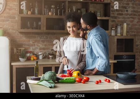 Man whispering in wife's ear while cooking Stock Photo