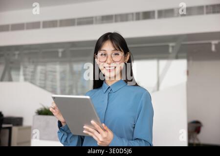 Happy smart young Asian professional in glasses typing on tablet Stock Photo