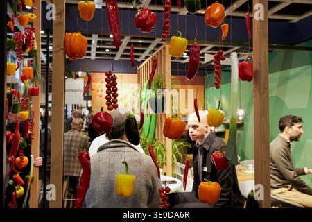 05.02.2026, Germany, Berlin, Berlin - Trade visitors exchange ideas at a trade fair stand at Fruit Logistica. Various types of vegetables hanging on w Stock Photo