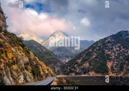 Winding mountain road passing through rugged canyon landscape beneath dramatic clouds. Stock Photo