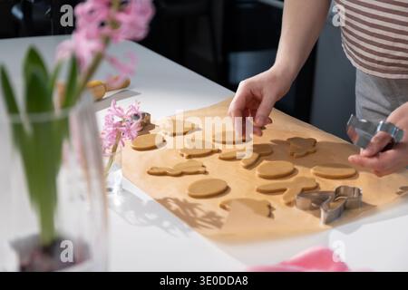 Hands are shaping gingerbread cookies in various Easter designs on a countertop in a cozy kitchen. Family members gather to help prepare for the holiday festivities and traditions. Stock Photo