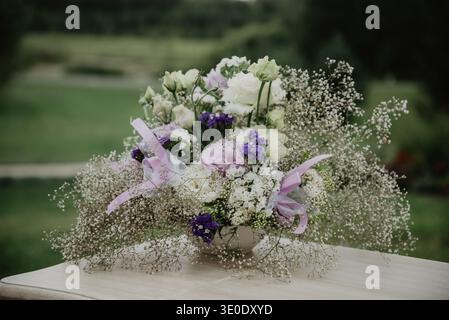 Romantic floral bouquet with white and purple flowers arranged in a vase on an outdoor table. Soft natural light and blurred garden background create Stock Photo