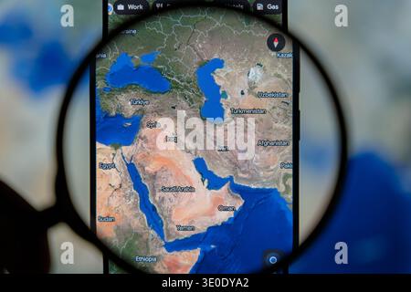 Magnifying glass focusing on a digital satellite map of the Middle East on a smartphone, displaying countries like Saudi Arabia, Iran, and Turkey for Stock Photo
