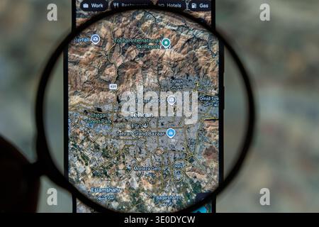 Magnifying glass over smartphone screen showing satellite map of Tehran Iran, searching for strategic locations and urban infrastructure on Google Stock Photo