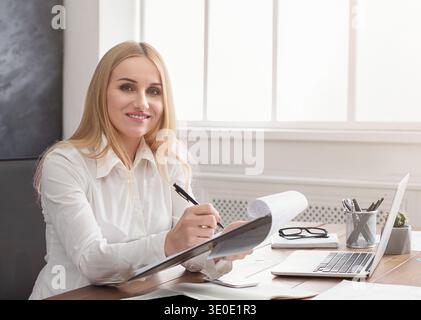 Young successful woman writing notes while sitting in office Stock Photo