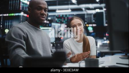 Diverse Professional Team Reviewing Investment Data in Global Brokerage Firm. Mentor Gestures Towards Advanced Financial Indices, Woman Engages in Discussion. Concept of Synergy of Multicultural Team. Stock Photo
