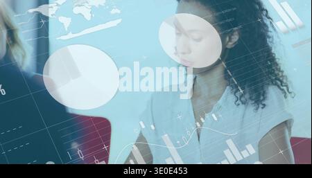 Analyzing curly-haired woman in light blouse reviewing charts at table, showing data overlays Stock Photo