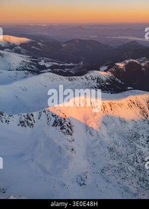 Aerial view of snow-covered peaks kissed by the warm glow of the setting sun over Dumbier, Nizke Tatry, Zilina Region, Slovakia. Stock Photo