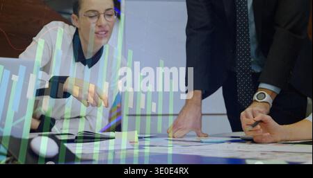 Reviewing three professionals in business attire analyzing charts at conference table, with laptop Stock Photo