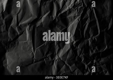 Crumpled black blank sheet as texture or background, long picture of folded dark paper, top view Stock Photo
