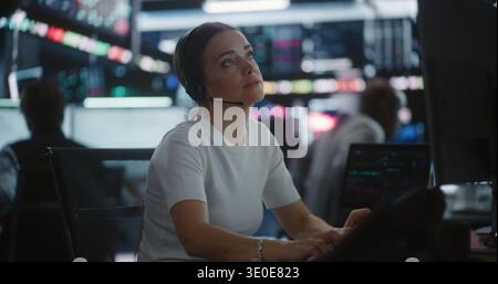 Female Trader Works in Modern Stock Exchange. Woman Interacts With Digital Tablet While Monitoring Complex Market Data Across Large Screens. Concept of Financial Analytics, Professional Multitasking. Stock Photo