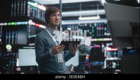 Successful Financial Analyst Surveying Real Time Trading Floor. Young Trader Stands in of High Tech Stock Exchange, Wearing Professional Headset and Corporate Lanyard. Concept of Top Tier Competence. Stock Photo