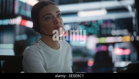 Serious Female Analyst Engaged in Deep Data Research High Tech Desk. Wearing Professional Headset, Woman Uses Tablet Track Asset Performance While Overseeing Display of Fluctuating Financial Indices. Stock Photo