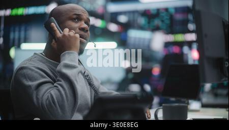 Professional African American Broker Closely Monitoring Charts and Calling Landline Phone Receiver. Man Delivers Urgent Market Update. Concept of Intensity Live Trading Operations in Stock Exchange. Stock Photo