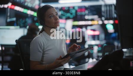 Female Trader Works in Modern Stock Exchange. Woman Interacts With Digital Tablet While Monitoring Complex Market Data Across Large Screens. Concept of Financial Analytics, Professional Multitasking. Stock Photo