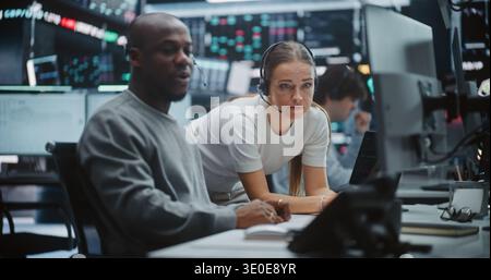 Two Professional Brokers Analyzing Big Data Trends on Multi Monitor Dashboard. Man Gestures Towards Specific Chart on Monitors While Woman Provides Input. Strategic Planning in Modern Fintech Office. Stock Photo