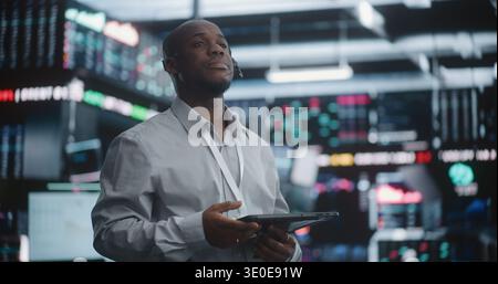 Focused Black Financial Expert Reviewing Real Time Trading Indices. Equipped Headset And Tablet, Man Monitors Global Market Fluctuations With Air of Authority And Expertise. Calm Under Pressure. Stock Photo