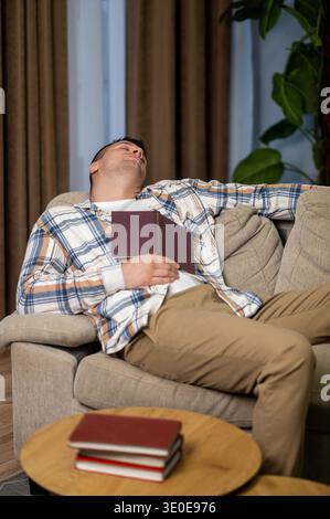 Tired man sleeping with book on sofa in modern living room interior Stock Photo