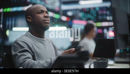 African American Investor Tracking Asset Performance in Innovative Trading Center. Man Focused on Digital Dashboard on Monitors and Digital Tablet. Intense Concentration in Global Finance Industry. Stock Photo