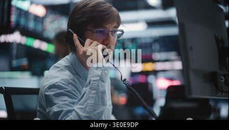 Professional Broker Taking Urgent Call on Landline Phone at Trading Desk. Man Coordinates Market Orders and Provides Real Time Consultation to Clients. Concept of Reliable Investment Consultation. Stock Photo