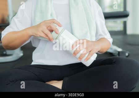 Cropped shot of mature woman sitting on floor with bottle  in health club, thirsty after training. Healthy concept. Stock Photo