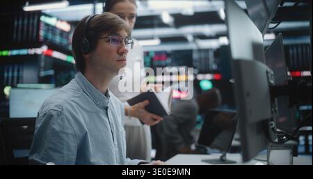 Financial Analysts Collaborating and Discussing Market Trends at Trading Desk. Male Trader in Glasses and Female Colleague With Headset Work Together Multi Monitor Workstation. Market Analysis. Stock Photo