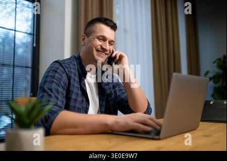 Happy man speaking on phone and working on laptop in contemporary office Stock Photo