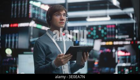 Successful Financial Analyst Surveying Real Time Trading Floor. Young Trader Stands in of High Tech Stock Exchange, Wearing Professional Headset and Corporate Lanyard. Concept of Top Tier Competence. Stock Photo
