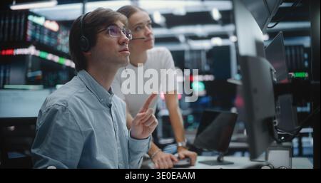 Financial Analysts Collaborating and Discussing Market Trends at Trading Desk. Male Trader in Glasses and Female Colleague With Headset Work Together Multi Monitor Workstation. Market Analysis. Stock Photo