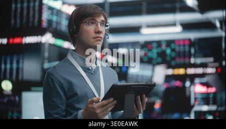 Investment Specialist Analyzing Stock Performance at Advanced Workstation, Standing on Live Trading Floor, Professional Interaction With Mobile Technology. Strategic Planning, Individual Leadership. Stock Photo
