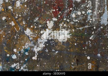 close-up of a messy artist's canvas featuring white paint splatters, multi-colored stains, and a gritty. Stock Photo