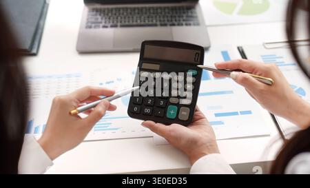 Financial Calculation. Two professionals using a calculator to analyze financial data and reports. Stock Photo