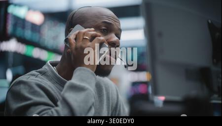 Close Up of Black Male Trader Using Smartphone to Coordinate Investment Strategies. Man Observing Big Data and Global Indices on Digital Displays. Communication and Modern Analytics in Exchange Hub. Stock Photo
