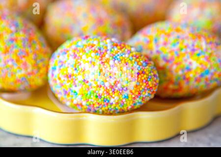 Colorful sprinkle-covered Easter egg on a yellow plate for playful spring celebration and sweet treat Stock Photo