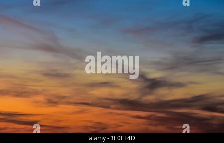 Intense contrast in the evening sky featuring heavy dark clouds divided by a brilliant glowing orange band of light at dusk. Stock Photo
