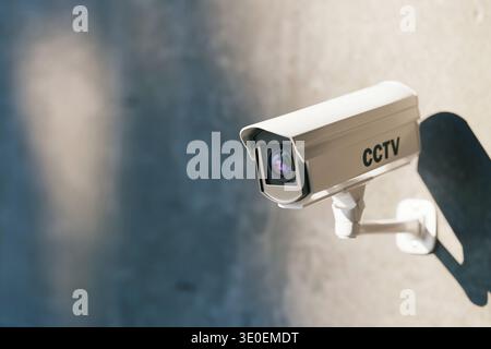 Modern white CCTV security camera mounted on a concrete wall. Professional surveillance system for urban safety, crime prevention and monitoring of pr Stock Photo