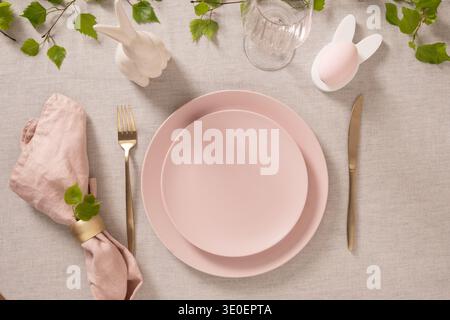 Easter table setting with pastel pink plate, decorative egg, quail eggs and golden cutlery on neutral linen background. Modern spring holiday decor, f Stock Photo