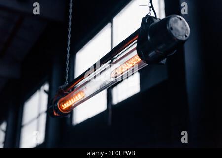 Industrial vintage tube light pendant. A close-up, low-light shot of an industrial-style tubular filament pendant lamp hanging by chains in workshop. Stock Photo