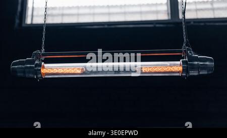 Symmetrical view of filament tube pendant. Industrial tubular pendant light suspended by chains, showcasing two glowing filaments inside a clear glass Stock Photo