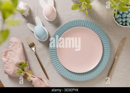 Spring Easter table composition with pastel plates, decorative eggs, linen napkin and fresh green leaves creating festive seasonal atmosphere. Stock Photo