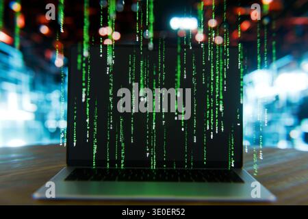modern laptop displaying a cascading green digital rain code on a dark screen, representing cybersecurity, hacking, and big data processing in a futur Stock Photo