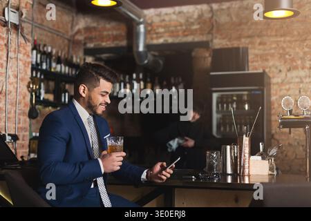 Young man sitting at bar counter and using smartphone Stock Photo