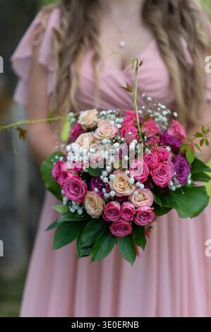 Close up of lush pink and cream rose bridal bouquet held in hands of a young bride wearing elegant beige dress. Romantic wedding moment with soft natu Stock Photo