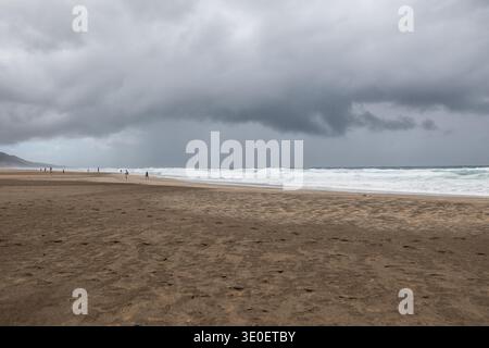Wide view of the dramatic coastline of Cofete beach with dark storm clouds over the Atlantic Ocean and the rugged mountains of the Jandia peninsula in Stock Photo